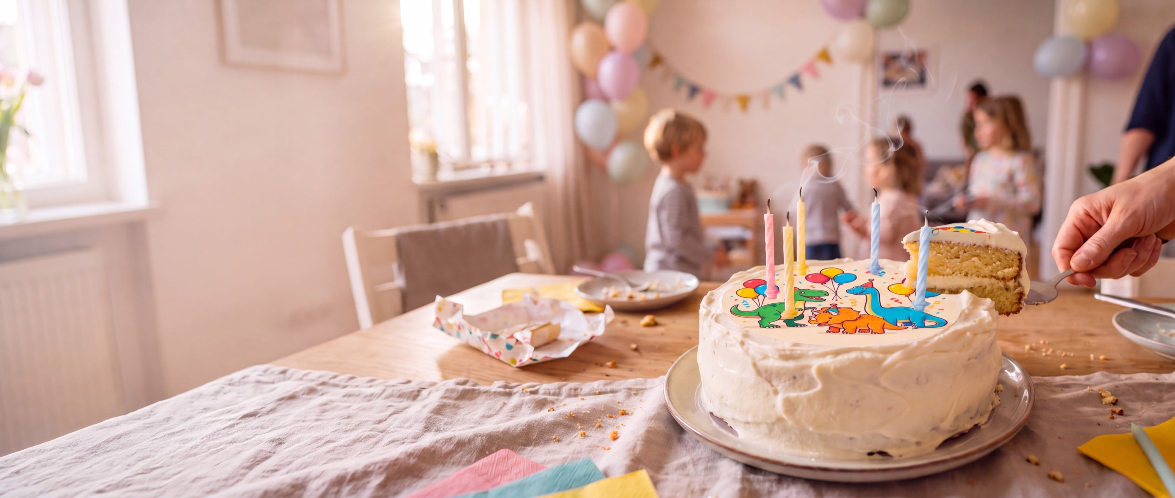 Angeschnittene Geburtstagstorte mit essbarem Dino-Aufdruck, fünf Kerzen und Kinderparty im Hintergrund